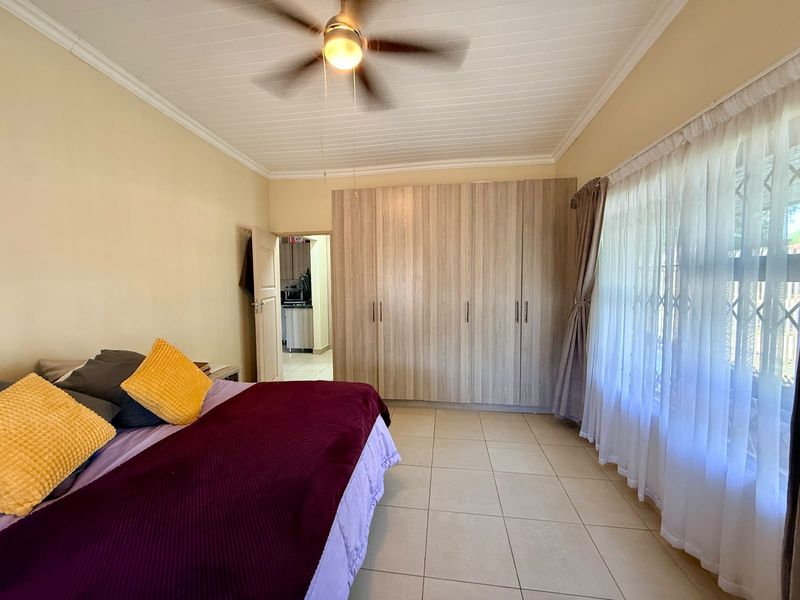 Spacious bedroom featuring built-in cupboards, tiled flooring, and a ceiling fan, with direct access to an adjoining room.