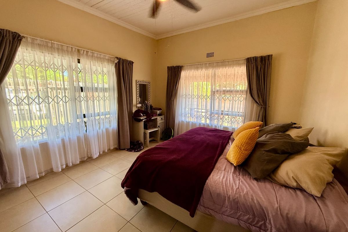 A well-lit bedroom featuring tiled flooring, a ceiling fan, and large windows fitted with security gates, offering a comfortable and functional living space.