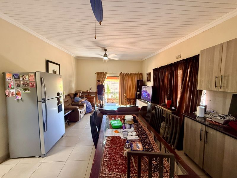Open-plan living and dining area featuring tiled floors, a tongue and groove ceiling, and a functional kitchen space with built-in cabinetry.