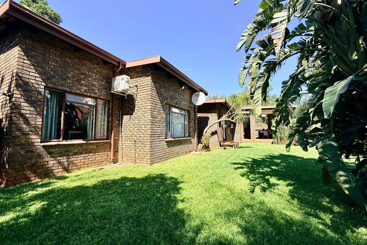A well-maintained rear exterior view of a face brick house featuring a spacious green lawn and a covered patio area.