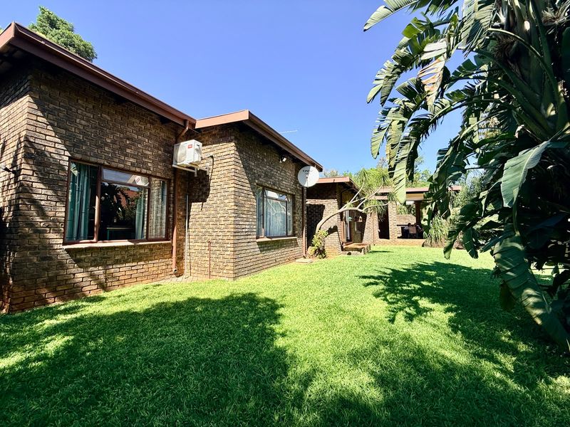 A well-maintained rear exterior view of a face brick house featuring a spacious green lawn and a covered patio area.