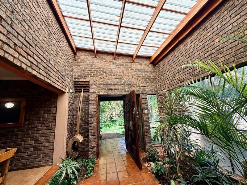 A unique, light-filled entrance hall featuring exposed brick walls, tiled flooring, and a translucent roof structure that creates an airy, indoor-outdoor atmosphere.