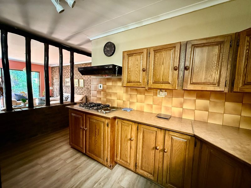 A functional kitchen featuring traditional wooden cabinetry, a gas hob with extractor fan, and a tiled backsplash, opening into the adjacent living area.