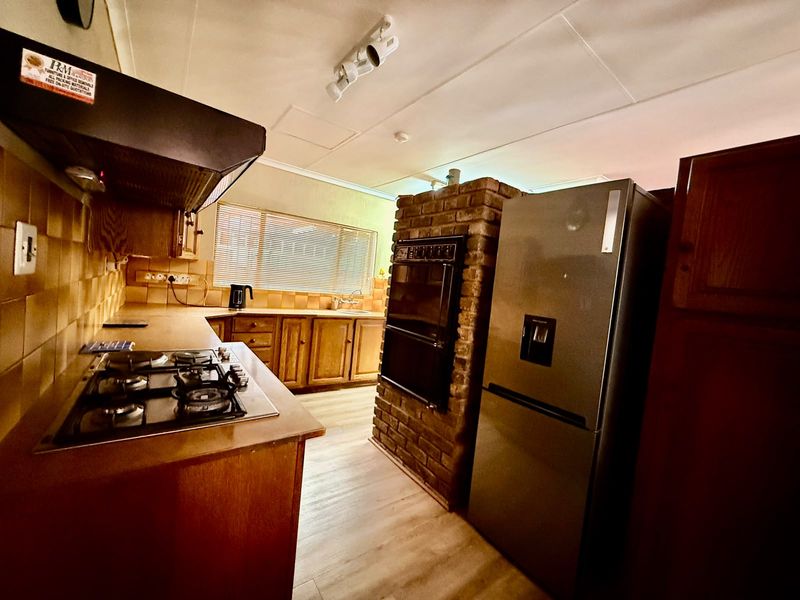 A functional kitchen featuring wooden cabinetry, a gas hob with extractor, and a unique brick-encased eye-level oven, offering a classic, lived-in aesthetic.