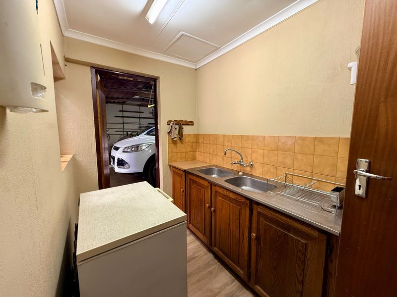 Functional scullery area featuring wooden cabinetry, a double stainless steel sink, and tiled splashbacks, providing convenient utility space with direct access to the garage.