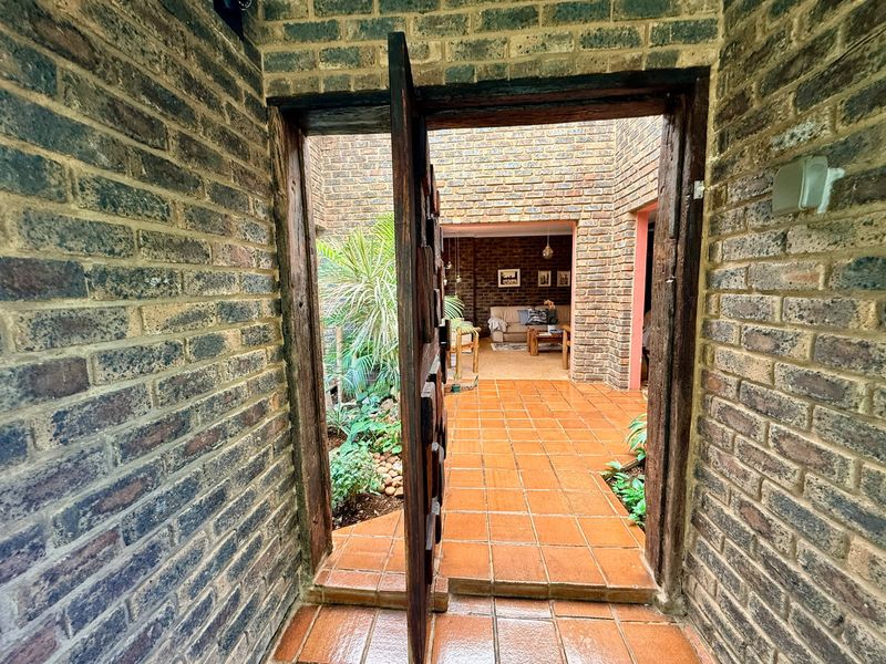 An inviting entrance featuring exposed brick walls and terracotta tiling, leading into a central courtyard and open-plan living area.