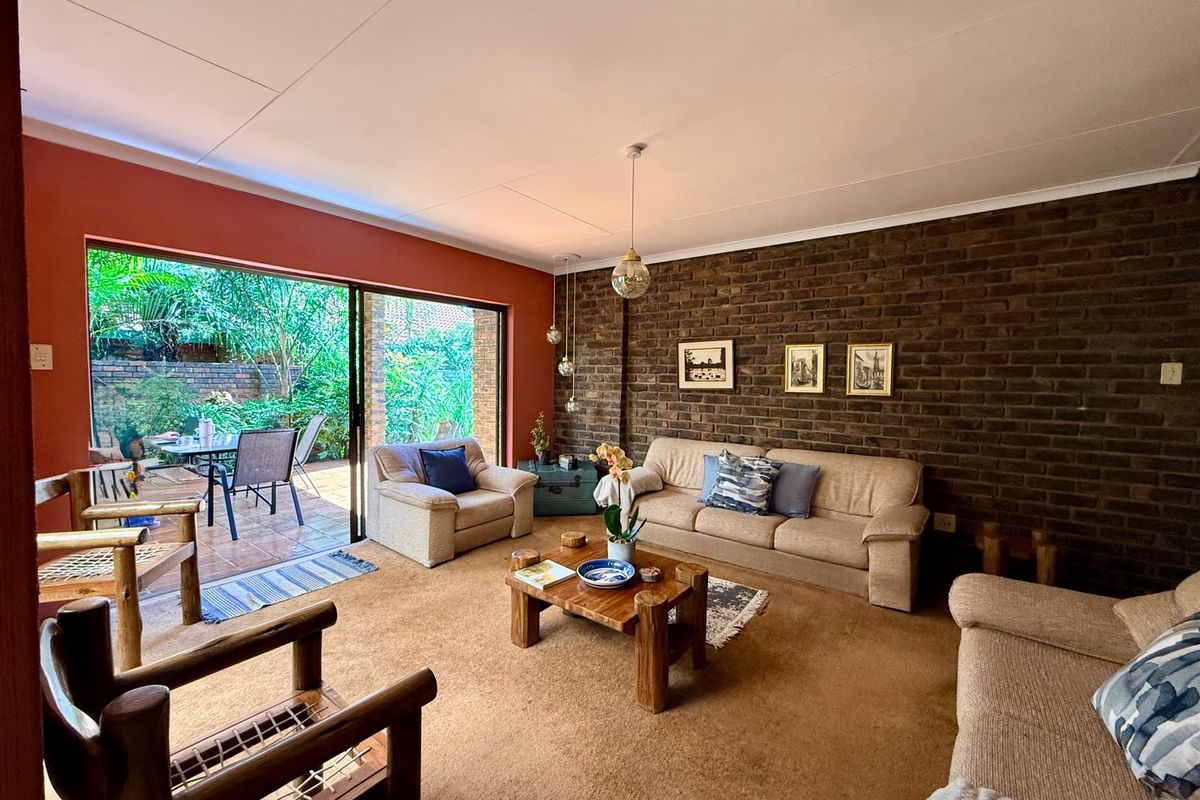Spacious living room featuring an exposed brick accent wall, carpeted flooring, and large sliding glass doors providing direct access to the outdoor patio area.