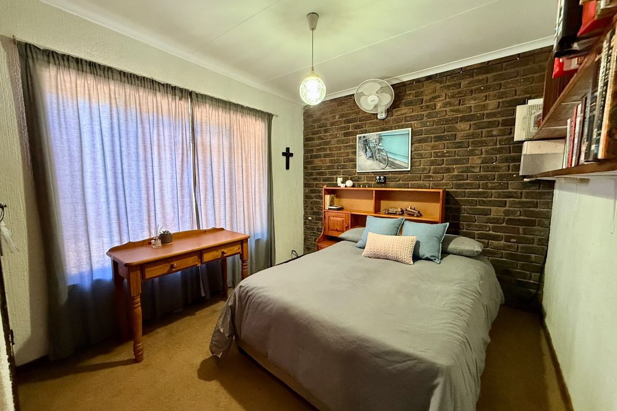 A bedroom featuring an exposed brick feature wall, carpeted flooring, and a ceiling fan, offering a cozy and rustic aesthetic.