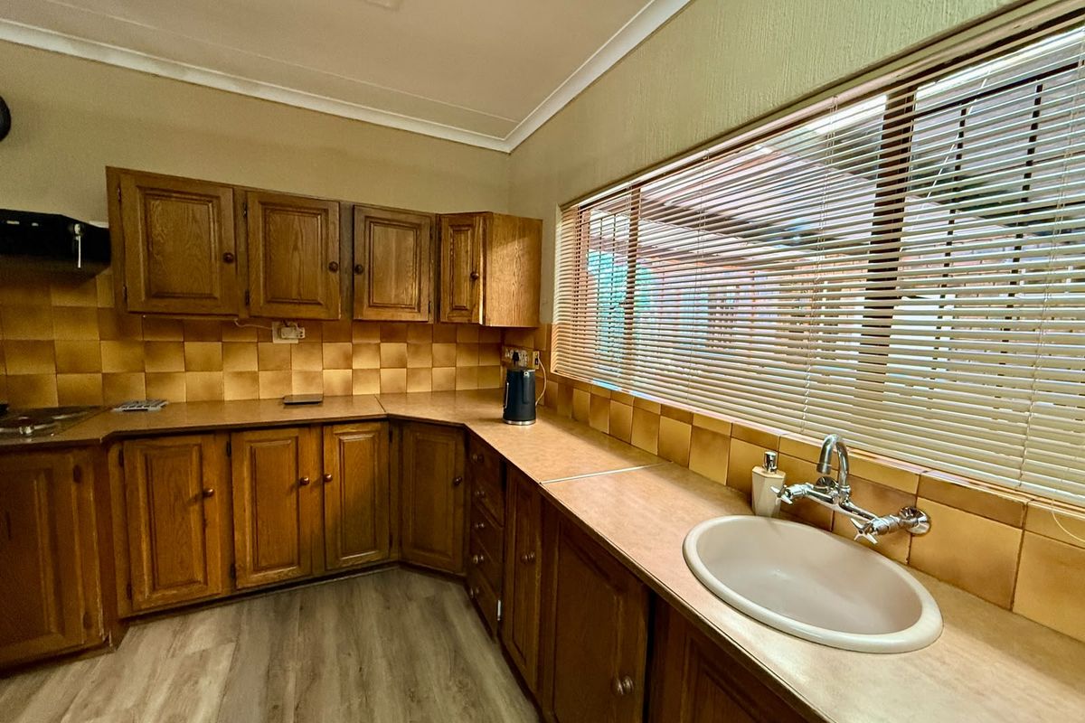 A functional kitchen featuring traditional wooden cabinetry, laminate countertops, a tiled backsplash, and a large window with venetian blinds.