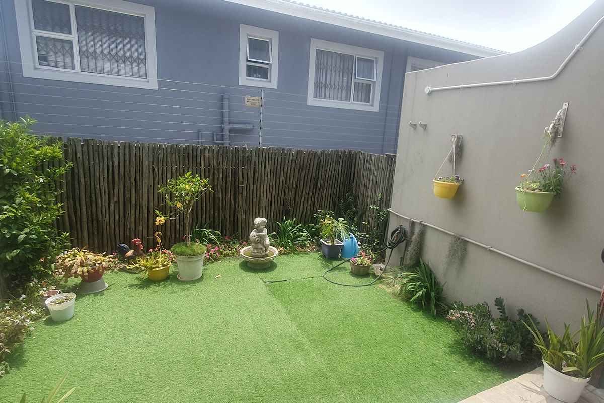 A compact rear courtyard featuring artificial turf, perimeter boundary walls, and security electric fencing.