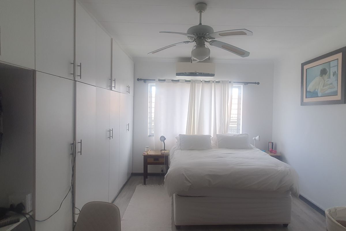 A well-maintained bedroom featuring extensive built-in cabinetry, a ceiling fan, and a wall-mounted air conditioning unit, providing ample storage and climate control.