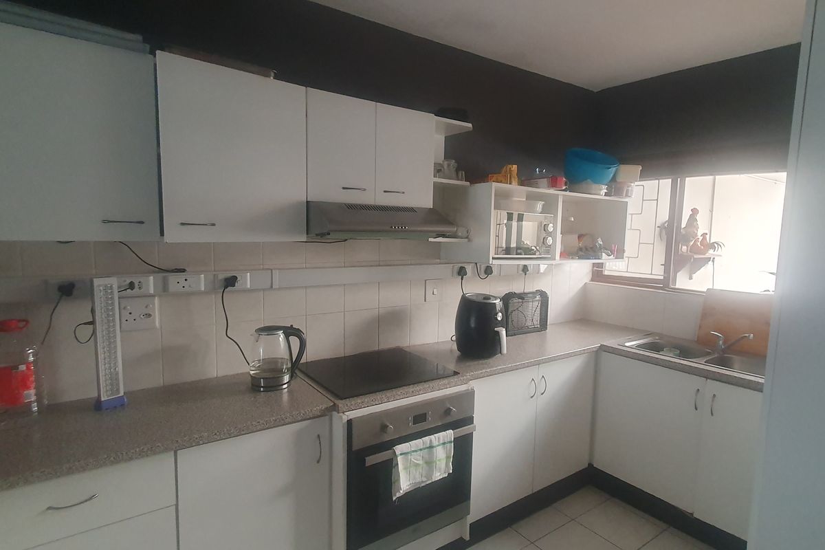 Functional kitchen featuring white cabinetry, laminate countertops, built-in oven, electric hob, extractor fan, and a double bowl sink with tiled backsplash.