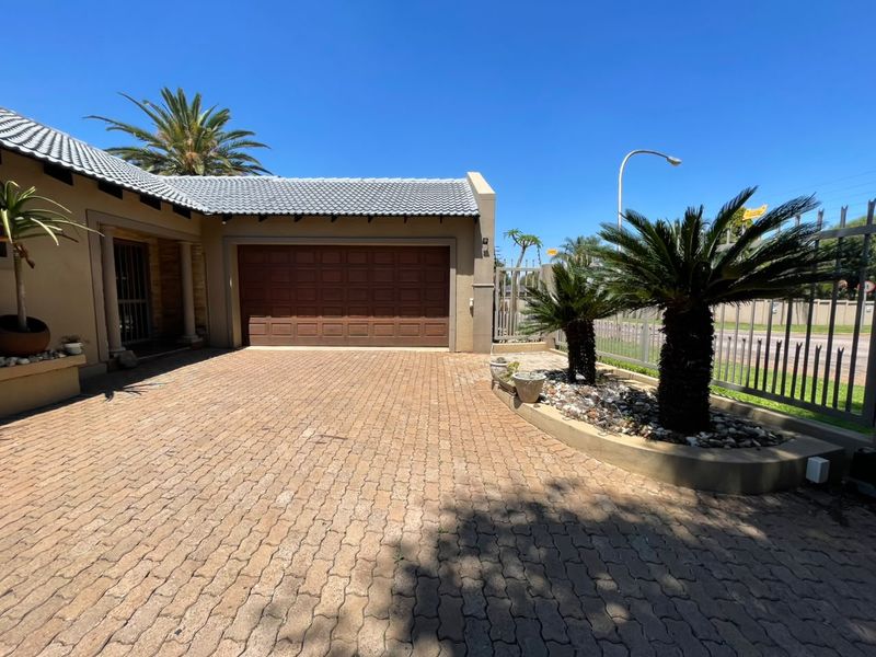 Front exterior view of the property featuring a paved driveway, double garage, and landscaped garden beds with perimeter fencing.