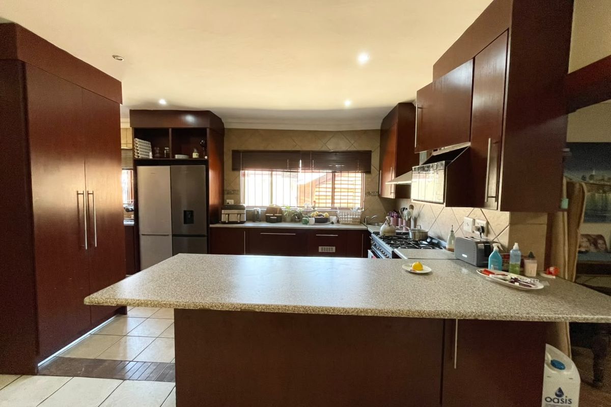 Spacious kitchen featuring dark wood cabinetry, a large central island with stone countertops, gas hob, and tiled flooring throughout.