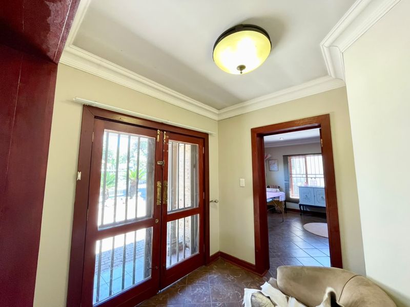 Entrance foyer featuring double wooden doors with security gates, crown molding, and tiled flooring, leading into an adjacent living space.