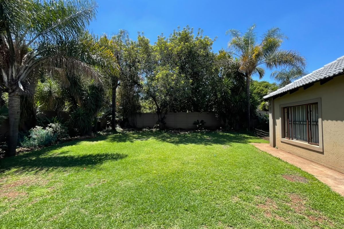 A well-maintained rear garden featuring a lush lawn, mature palm trees, and a secure precast boundary wall, adjacent to the home's exterior wall.