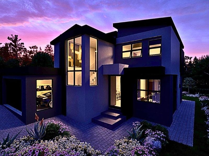 A modern two-story residential home featuring a paved driveway, landscaped garden, and large windows, captured during twilight.
