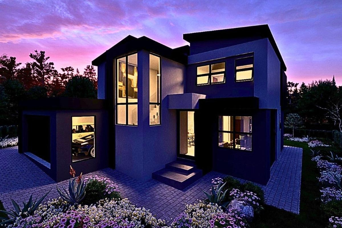 A modern two-story residential home featuring a paved driveway, landscaped garden, and large windows, captured during twilight.