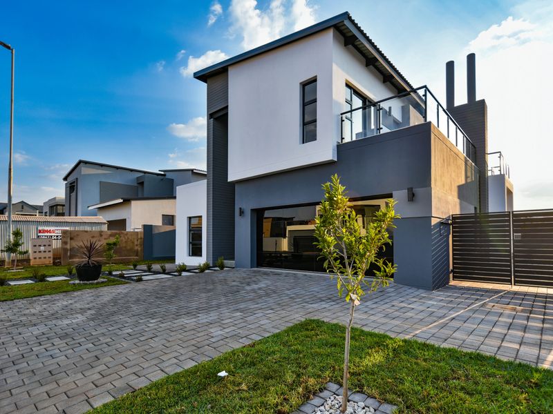 Modern double-story residential property featuring a paved driveway, double garage, and an upper-level balcony with glass balustrades.