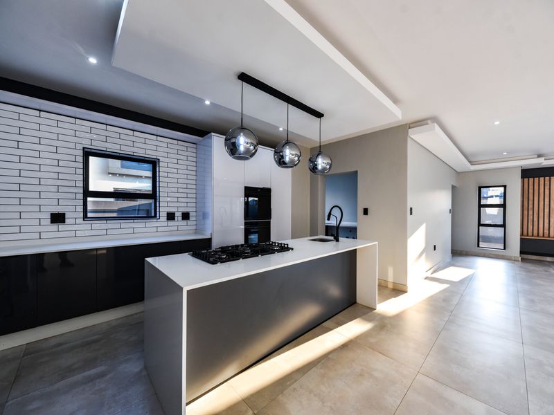 Modern open-plan kitchen featuring a central island with gas cooktop, sleek cabinetry, subway tile backsplash, and high-end finishes in a bright, spacious layout.