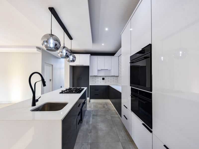 Modern kitchen featuring a central island with gas hob, sleek high-gloss cabinetry, integrated double ovens, and a stylish subway tile backsplash.