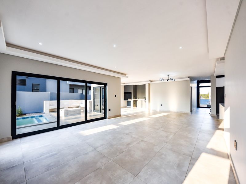 Spacious open-plan living area featuring large format floor tiles, recessed lighting, and seamless flow to an outdoor patio with a pool.
