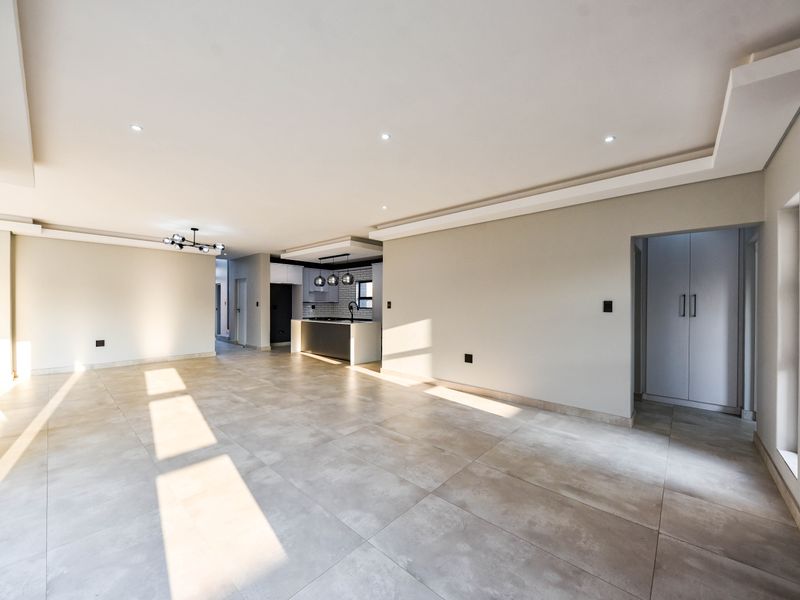 Spacious open-plan living area featuring modern tiled flooring, recessed ceiling lights, and a sleek kitchen with a central island and built-in cabinetry.