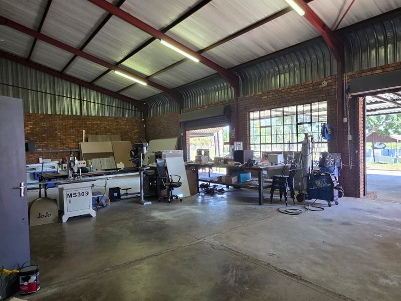 Spacious industrial utility workshop featuring exposed steel trusses, brick walls, concrete flooring, and large roller shutter access, suitable for various commercial or hobbyist uses.