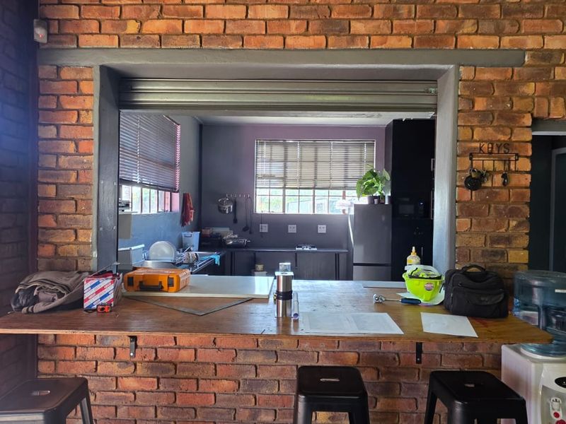 Open plan area featuring exposed brick walls, a functional pass-through window with a roller shutter, and a built-in breakfast bar connecting to the kitchen.