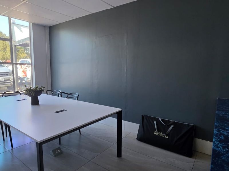 A bright office space featuring large windows, tiled flooring, a built-in counter, and a modern dark accent wall.