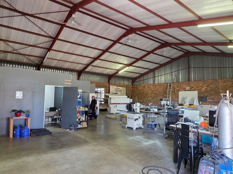Spacious industrial utility area featuring exposed steel roof trusses, facebrick walls, and durable concrete flooring, suitable for workshop or storage use.