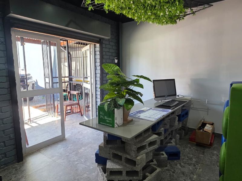 A functional office space featuring exposed brick walls, tiled flooring, and a sliding glass door providing access to the exterior.