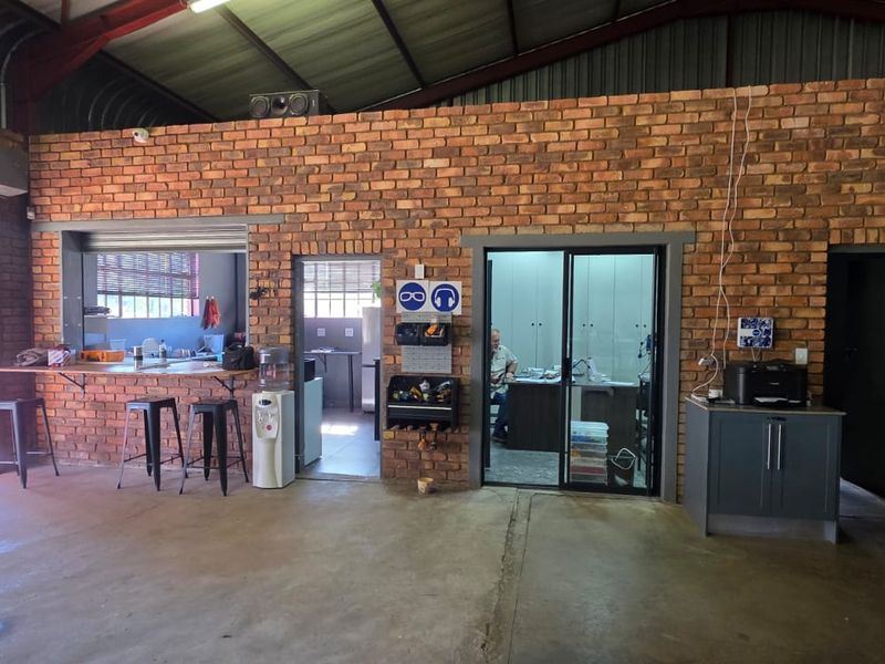 A spacious industrial-style utility area featuring exposed brick walls, concrete flooring, and a high corrugated metal ceiling with integrated office and service access points.