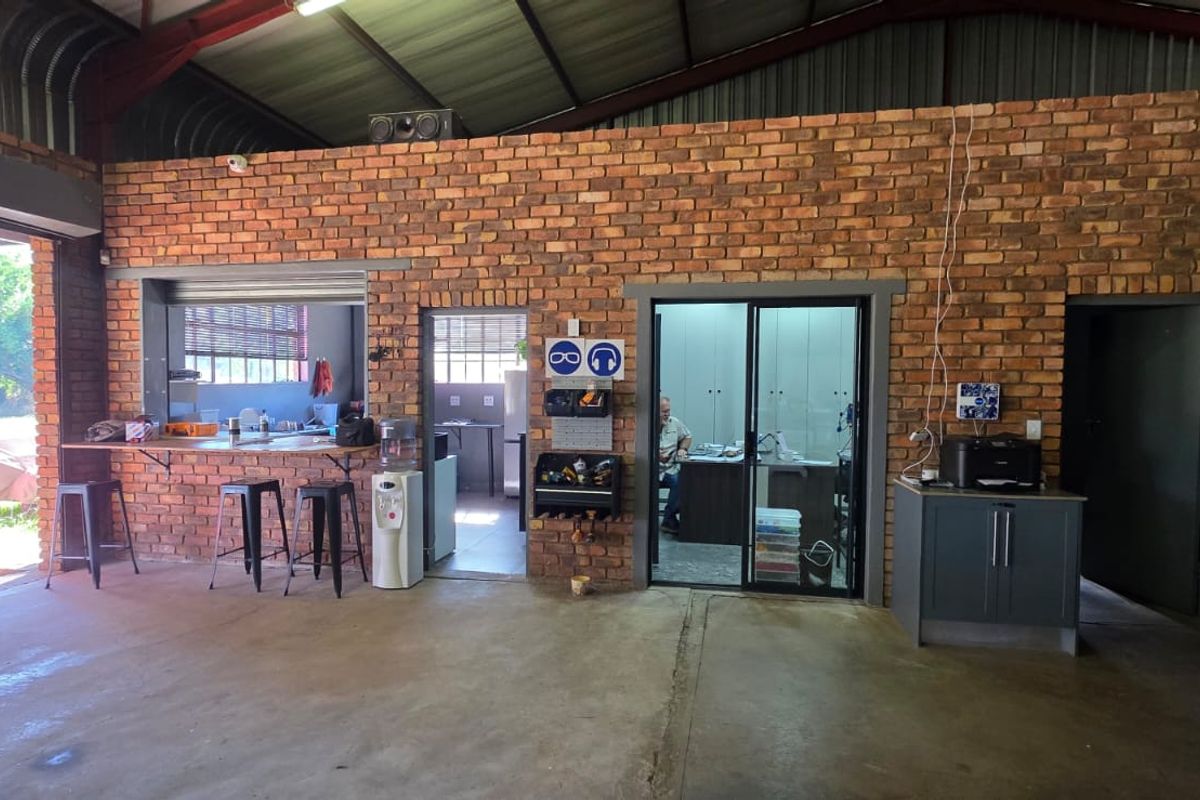 A spacious industrial-style utility area featuring exposed brick walls, concrete flooring, and a high corrugated metal ceiling with integrated office and service access points.
