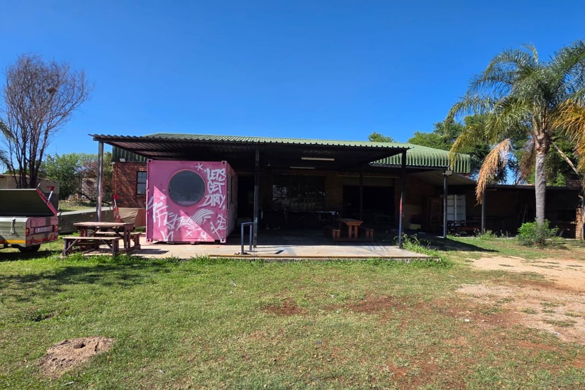 Rear view of the property featuring a large covered patio area with a concrete slab and brick structure, set within a spacious garden.