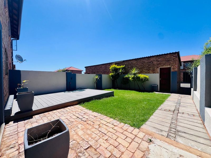 A well-maintained rear garden featuring a composite deck, brick-paved pathways, and a neat lawn enclosed by boundary walls.