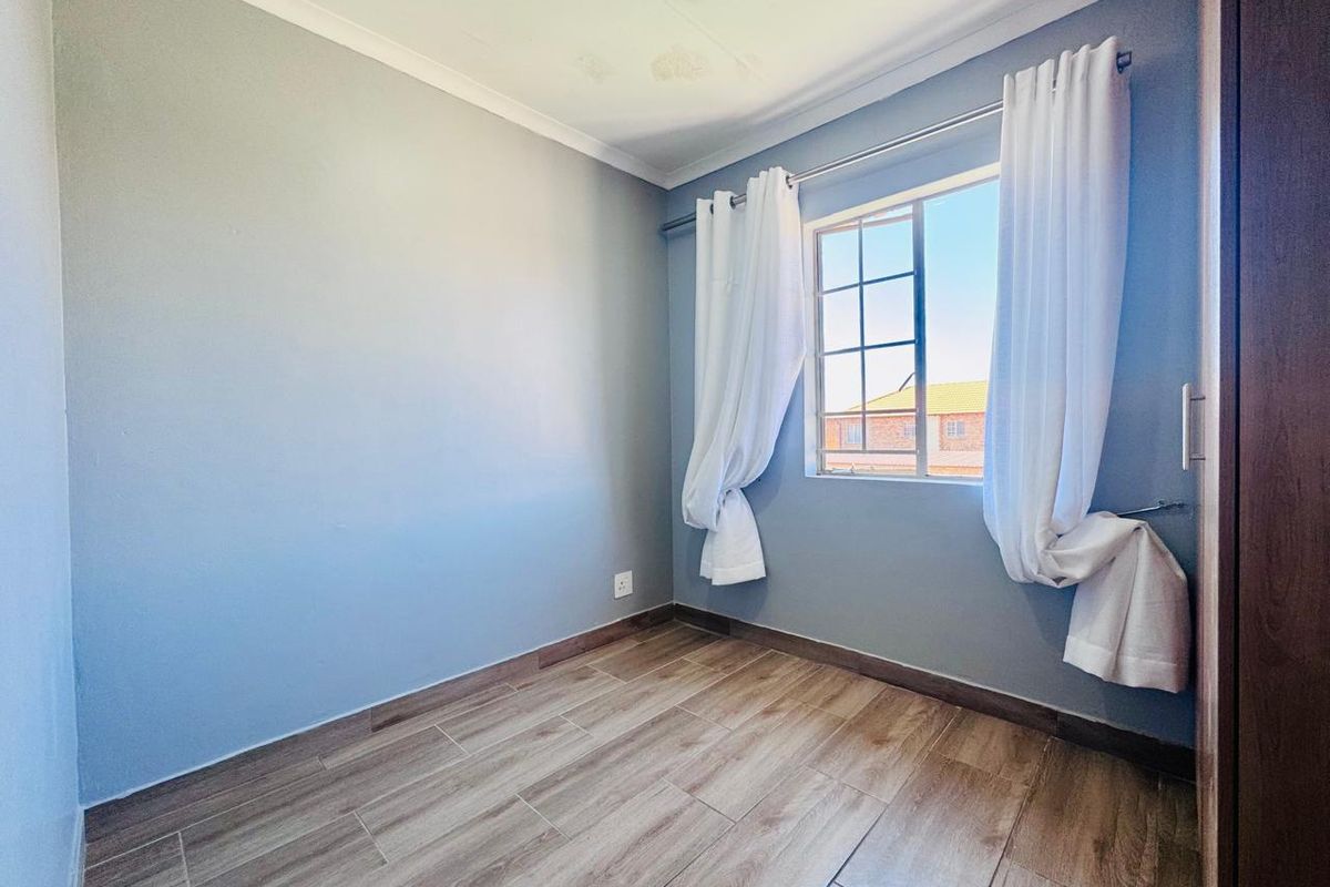 An empty bedroom featuring laminate flooring, a built-in cupboard, and a window with burglar bars. Note visible water staining on the ceiling.