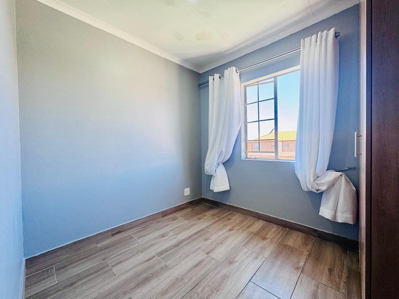 An empty bedroom featuring laminate flooring, a built-in cupboard, and a window with burglar bars. Note visible water staining on the ceiling.