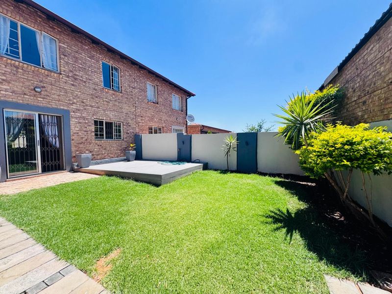 A well-maintained rear garden featuring a raised timber deck, brick facade townhouse exterior, and a secure boundary wall.