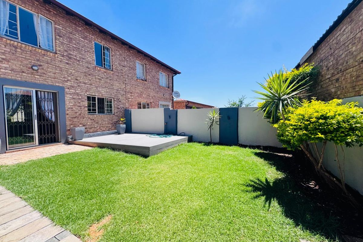 A well-maintained rear garden featuring a raised timber deck, brick facade townhouse exterior, and a secure boundary wall.