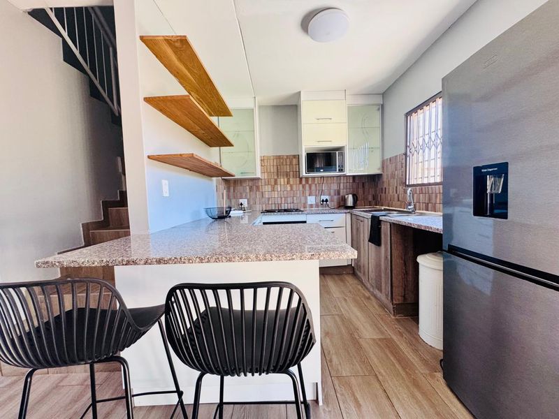 Modern kitchen featuring granite countertops, floating wooden shelving, tiled backsplash, and built-in cabinetry, conveniently located adjacent to the staircase.