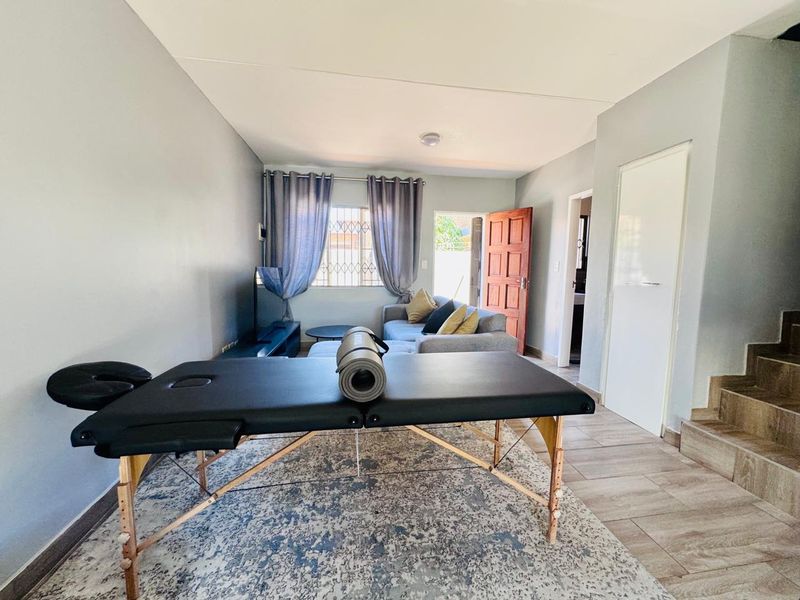 A living area featuring tiled flooring, a staircase, and access to an exterior door with security gate.