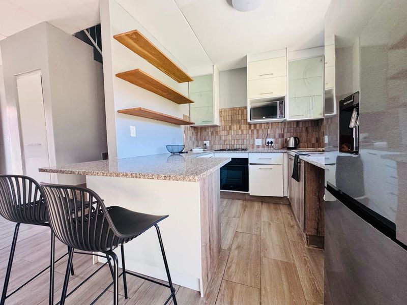 Modern kitchen featuring granite countertops, built-in oven and hob, floating wooden shelving, and stylish tiled backsplash with ample cabinetry.