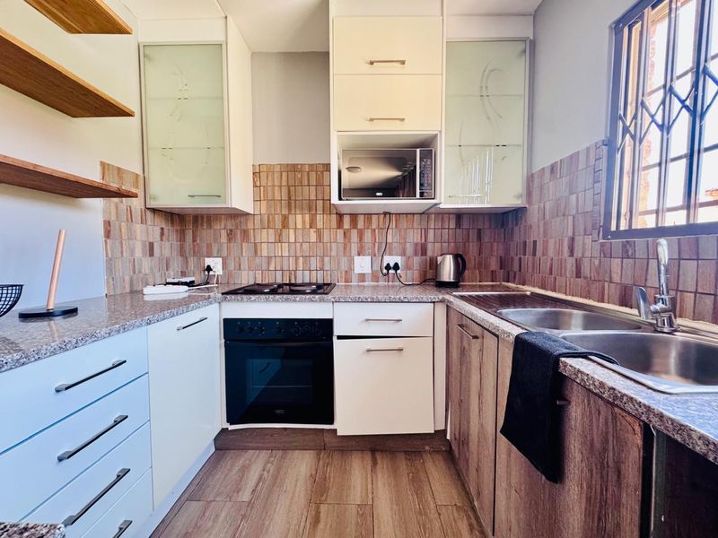 A functional kitchen featuring granite countertops, built-in oven and hob, double sink, and ample cabinetry with a decorative tiled backsplash.
