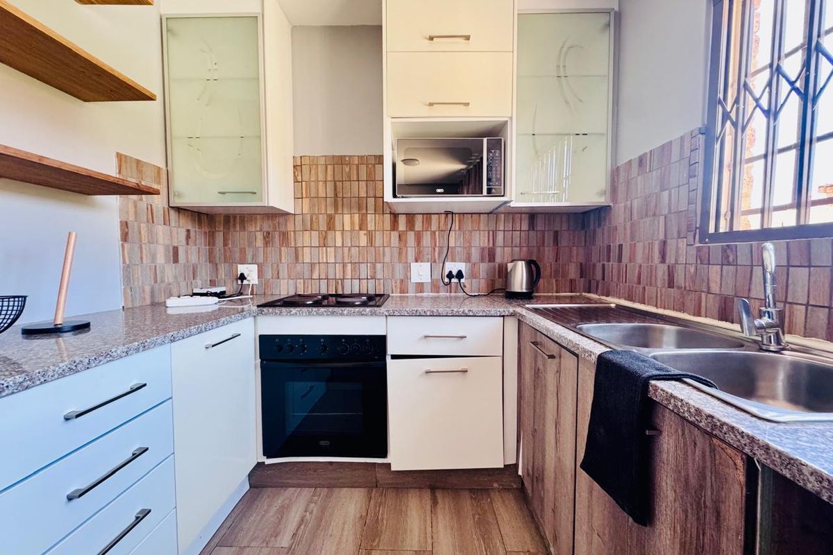 A functional kitchen featuring granite countertops, built-in oven and hob, double sink, and ample cabinetry with a decorative tiled backsplash.