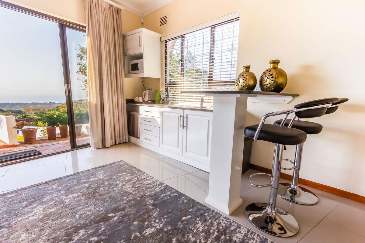 A compact kitchenette featuring white cabinetry, a breakfast bar, and sliding glass doors that open to an outdoor patio area.