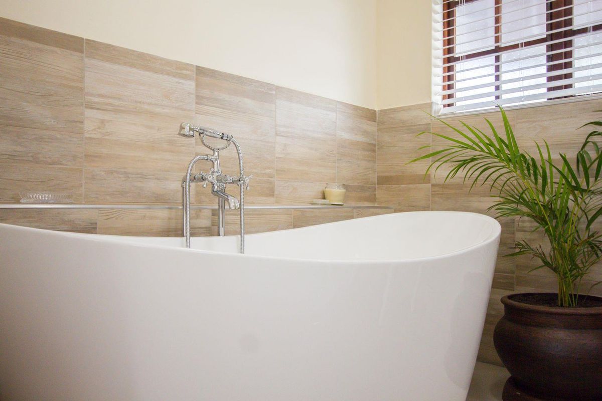 A modern bathroom featuring a freestanding white bathtub with chrome floor-mounted mixer tap and neutral wood-look wall tiling.