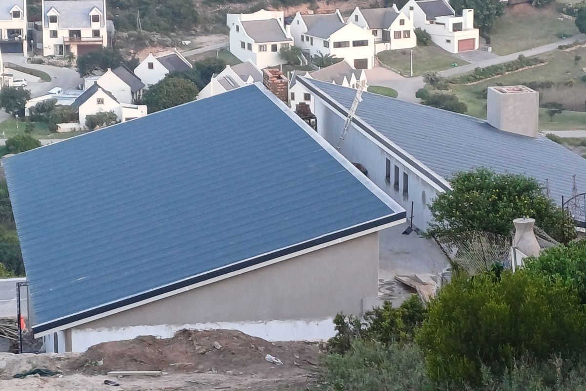 An elevated view of the duet property featuring modern pitched metal roofing, chimneys, and surrounding residential estate landscape.