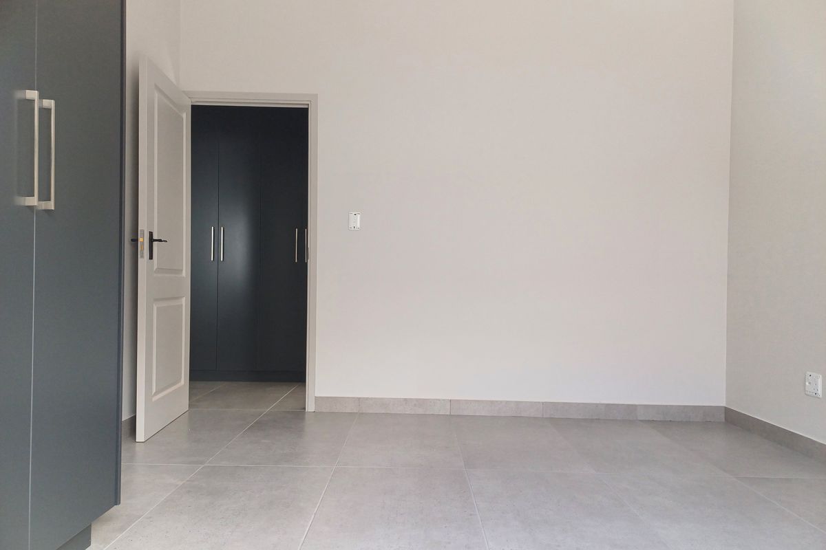 A bright, modern bedroom featuring neutral tiled flooring, built-in dark grey cabinetry, and a clean, minimalist aesthetic.