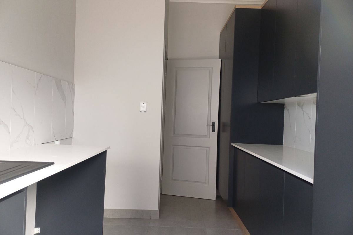 Modern kitchen featuring dark cabinetry, white stone countertops, and marble-effect tiled splashbacks, complemented by neutral floor tiles and a classic interior door.